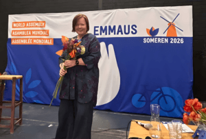 Carina Aaltonen står framför Emmaus Internationals banér, blommor i handen som ny ordförande