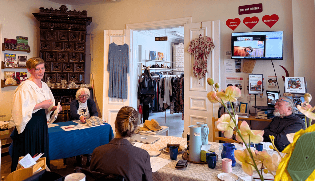 Svalornas ordförande inleder årsmötet i Svalornas secondhandbutik framför ett tiotal medlemmar