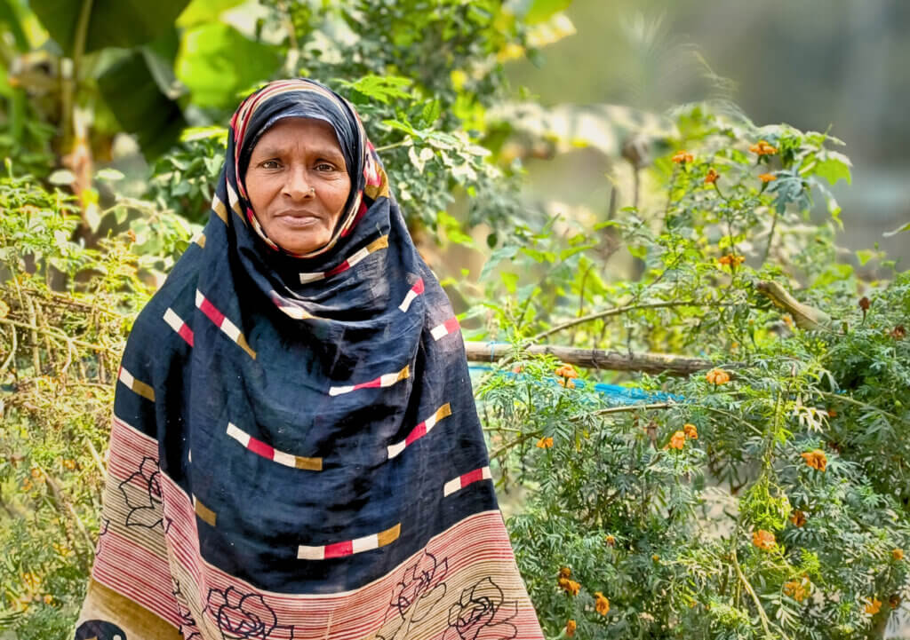 Joytun står framför ett buskage i sin egna odling